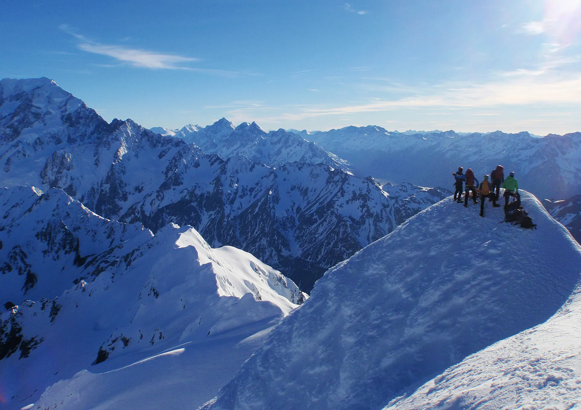 A rope team on a summit ridge, mountains stretching to the horizon